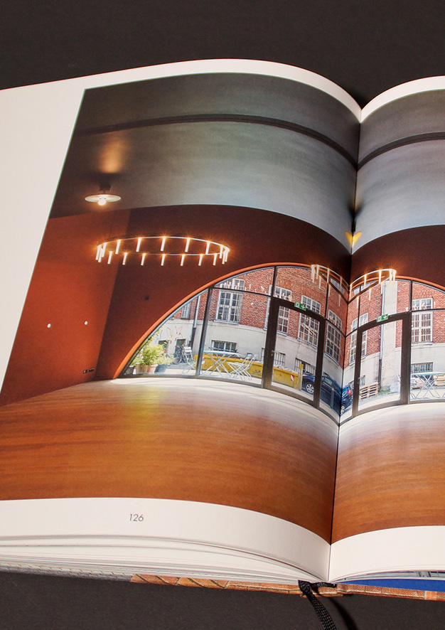 Aufgeschlagene Buchseite mit Blick aus dem holzgetäfelten Interieur durch einen Rundbogen nach draußen.