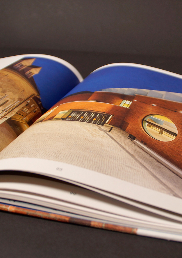 Aufgeschlagene Buchseite: Eindruck des Interieurs mit Holzboden und -rahmen, betongrauen Elementen und blauer Decke mit kreisförmig eingelassenen Leuchten.