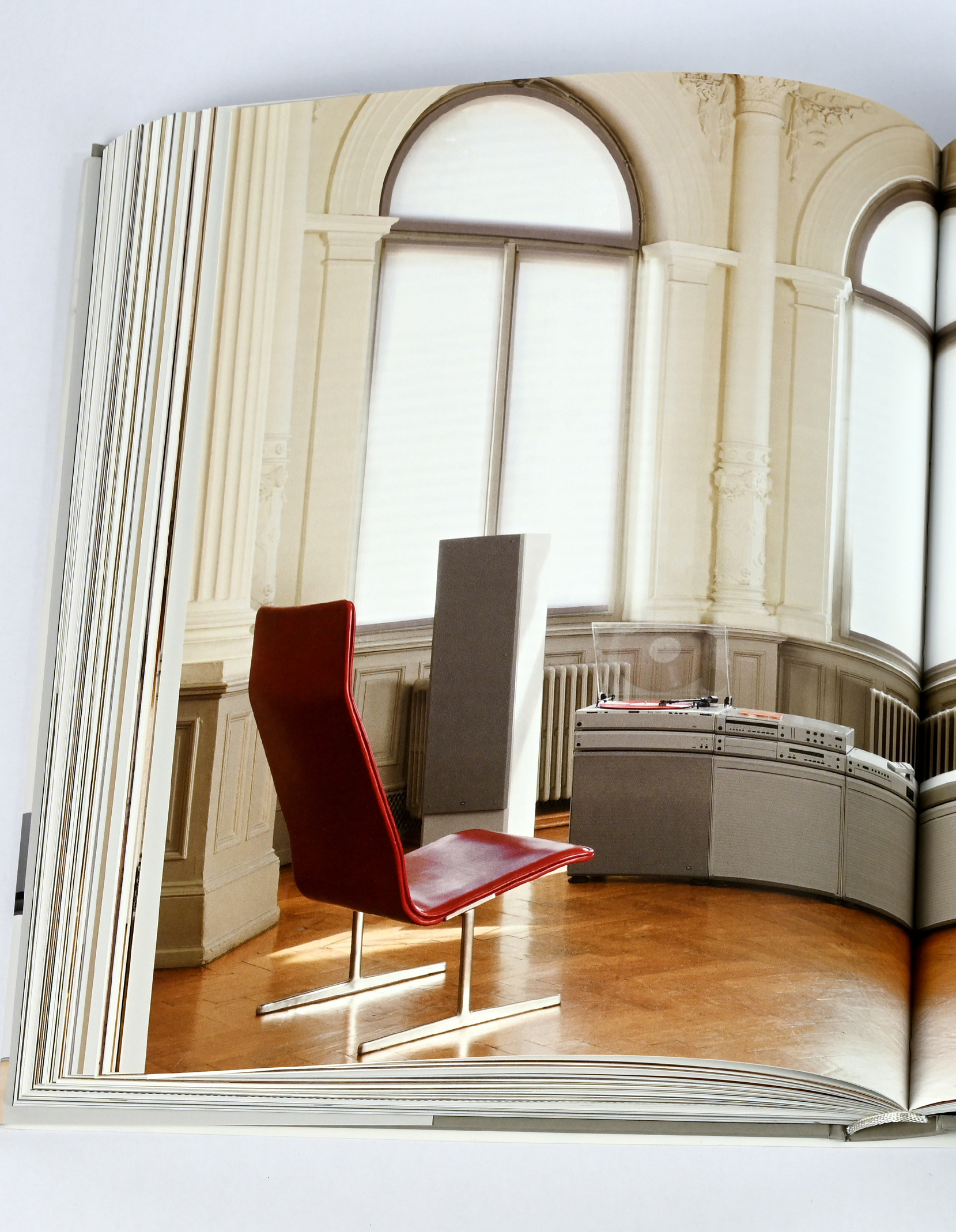 Aufgeschlagene Buchseite: In hellem Altbau fotografierte nebeneinanderstehende Braun Audio-Anlagen mit rotem Stuhl und Lautsprecherbox.
