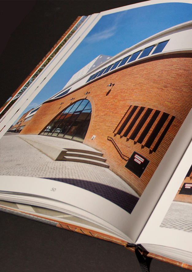Aufgeschlagene Buchseite mit Frontfassade aus anderer Richtung. Ein kleiner Treppenaufgang führt zu einem verglasten Rundbogen mit Eingang.